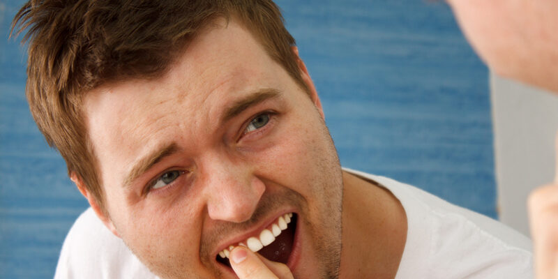 Man looks in the mirror at his damaged tooth